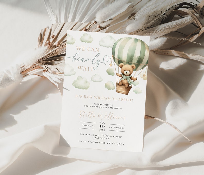 May include: A baby shower invitation with a watercolor illustration of a teddy bear in a hot air balloon. The invitation says "We can bearly wait" for baby William to arrive. The event is scheduled for August 10th at 12 o'clock at Bluebell Cafe.