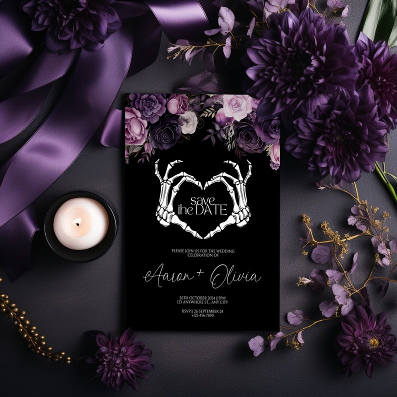 May include: A black and white save the date card with a floral design. The card features a skeleton hand making a heart shape with the text "save the date" inside. The text "Please join us for the wedding celebration of Aaron + Olivia" is below the heart. The date, time, and location of the wedding are listed below the names.