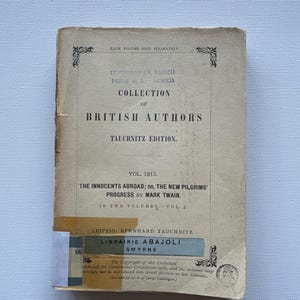 May include: A vintage book cover with the title "The Innocents Abroad; Or, The New Pilgrims' Progress by Mark Twain." The book is part of the "Collection of British Authors" series, published by Bernhard Tauchnitz in Leipzig. The book is volume 1813 and is in two volumes.