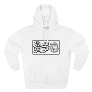 Puede incluir: Sudadera con capucha blanca con bolsillo delantero y capucha con cordón. La parte delantera presenta un gráfico en blanco y negro con las palabras "Dump Trump" y una ilustración de un cubo de basura guiñando un ojo.