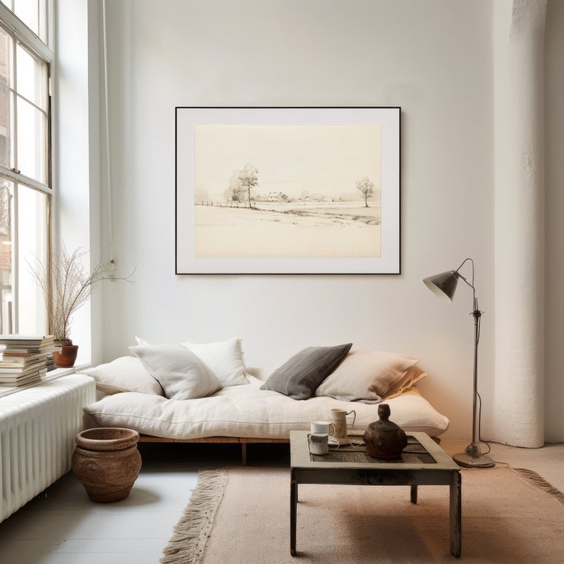 May include: A black framed print of a minimalist landscape drawing hangs above a white linen futon with a wooden frame. The futon is styled with white and gray throw pillows. A wooden coffee table with a rustic finish sits in front of the futon. A floor lamp with a black shade stands next to the futon.