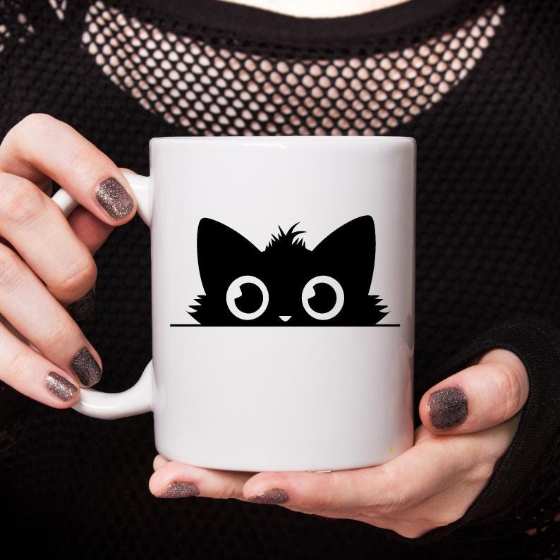 K&ouml;nnte beinhalten: Wei&szlig;e Keramiktasse mit einer schwarzen Silhouette einer Katze, die &uuml;ber den Rand schaut. Die Katze hat gro&szlig;e, runde Augen.