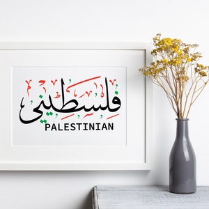 May include: A white framed print with the Arabic word for "Palestinian" written in black, red, and green. The word is written in a stylized calligraphy font. The word "Palestinian" is written in English below the Arabic word.