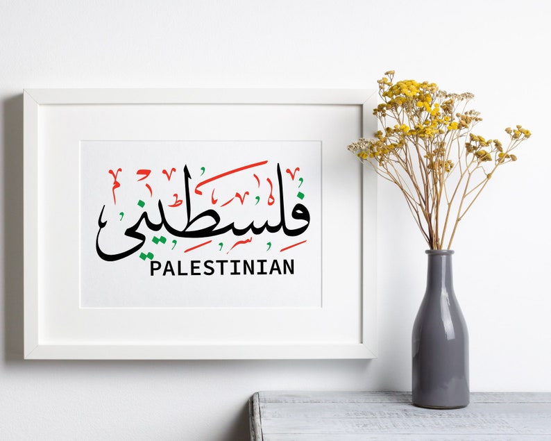 May include: A white framed print with the Arabic word for "Palestinian" written in black, red, and green. The word is written in a stylized calligraphy font. The word "Palestinian" is written in English below the Arabic word.