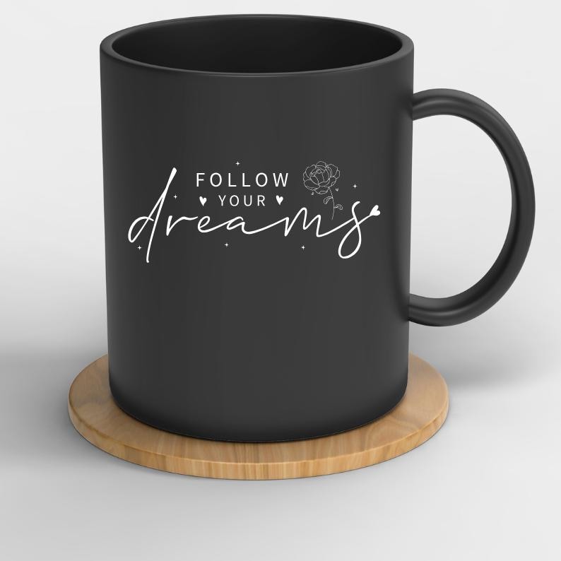 May include: Black ceramic mug with a white design that says "Follow your dreams" with a small rose illustration. The mug is sitting on a wooden coaster.