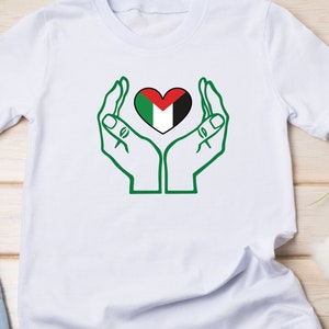 May include: White t-shirt with a green outline of two hands holding a heart-shaped Palestinian flag.