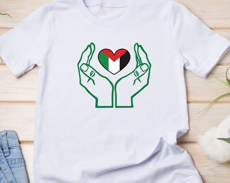 May include: White t-shirt with a green outline of two hands holding a heart-shaped Palestinian flag.