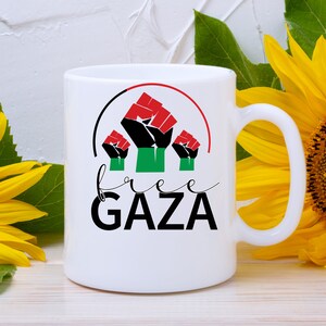 May include: White ceramic mug with a black, red, and green fist graphic and the text "free GAZA" in black.