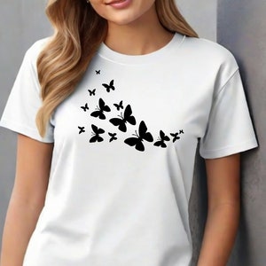 Puede incluir: Camiseta blanca con una silueta negra de una bandada de mariposas volando en diagonal.