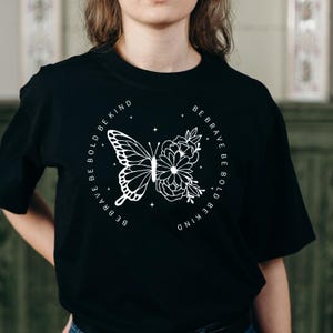 May include: Black t-shirt with a white graphic design of a butterfly and flowers. The text around the design reads "Be Brave Be Bold Be Kind".