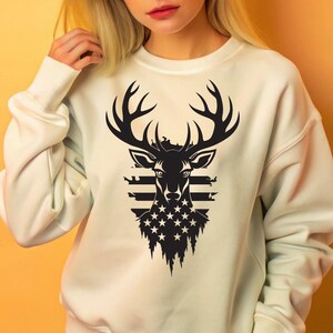 May include: White sweatshirt with a black and white graphic of a deer head with antlers. The deer head is superimposed over an American flag design.
