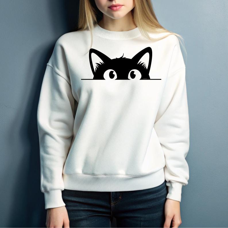 K&ouml;nnte beinhalten: Wei&szlig;er Pullover mit einer schwarzen Katze, die &uuml;ber den Rand schaut. Die Katze hat gro&szlig;e Augen und ein schlichtes Design.