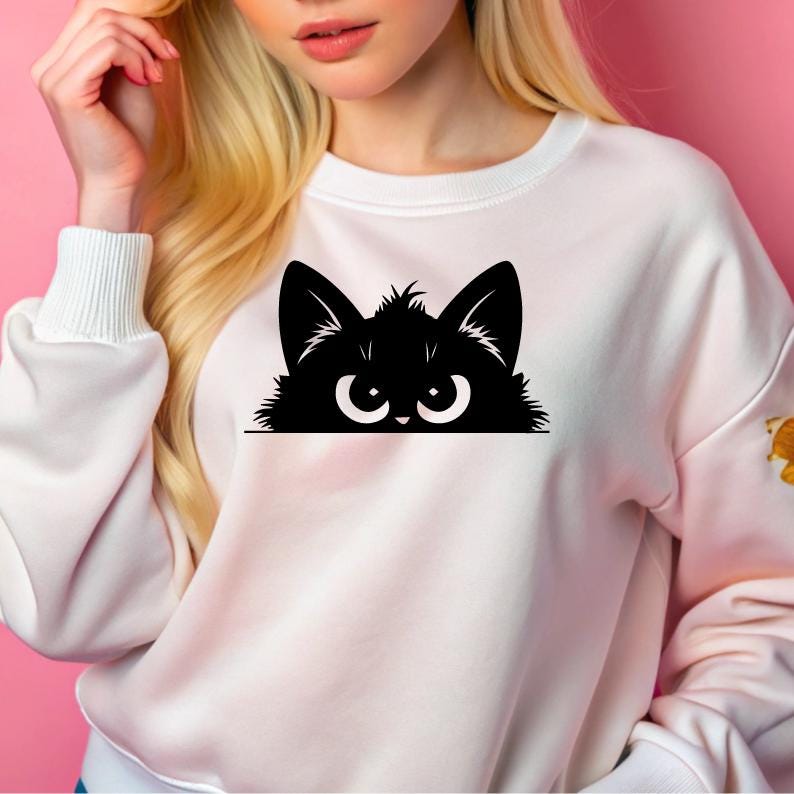 K&ouml;nnte beinhalten: Wei&szlig;er Pullover mit einer schwarzen Katze, die &uuml;ber den oberen Rand schaut. Die Katze hat gro&szlig;e Augen und einen ernsten Ausdruck.