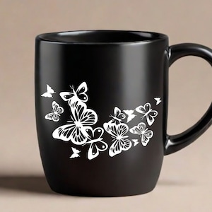 Puede incluir: Taza de caf&eacute; de cer&aacute;mica negra con un dise&ntilde;o de mariposa blanca. Las mariposas est&aacute;n agrupadas en el lateral de la taza.