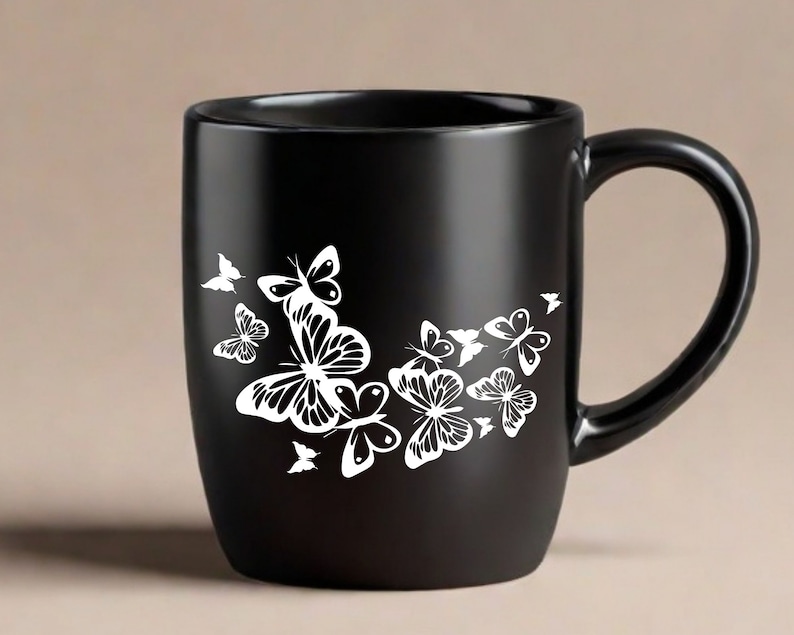 Puede incluir: Taza de caf&eacute; de cer&aacute;mica negra con un dise&ntilde;o de mariposa blanca. Las mariposas est&aacute;n agrupadas en el lateral de la taza.