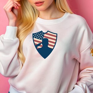 May include: White sweatshirt with a blue shield design featuring a silhouette of a person saluting in front of an American flag.