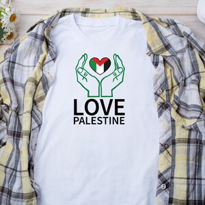 May include: White t-shirt with a green, black, and white heart with hands around it. The text "LOVE PALESTINE" is below the heart.
