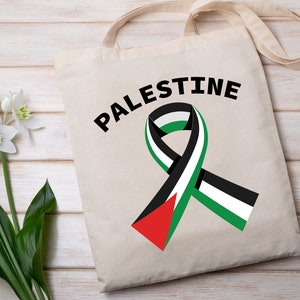 May include: A white tote bag with black handles and the word "PALESTINE" printed in black. A green, white, and black ribbon is printed on the bag.
