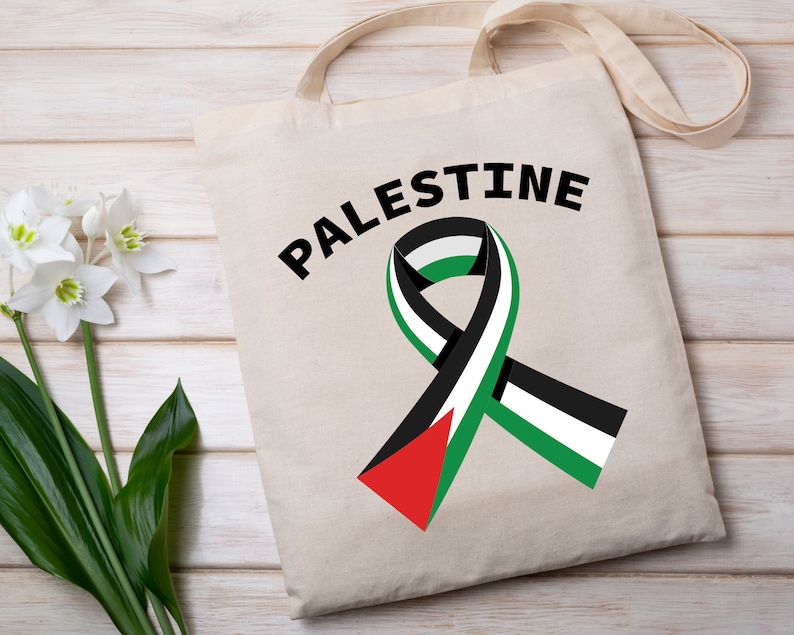 May include: A white tote bag with black handles and the word "PALESTINE" printed in black. A green, white, and black ribbon is printed on the bag.