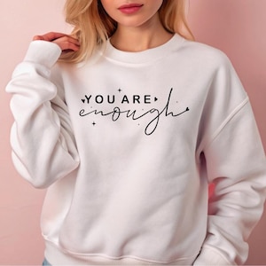 May include: White sweatshirt with the text "YOU ARE enough" in black script with small hearts and stars.