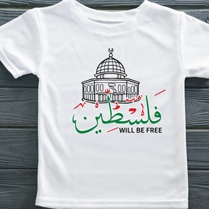 May include: White t-shirt with a black line drawing of the Dome of the Rock, a mosque in Jerusalem. The Arabic text "فلسطين" (Palestine) is written in green and red, and the English text "WILL BE FREE" is written in black below.