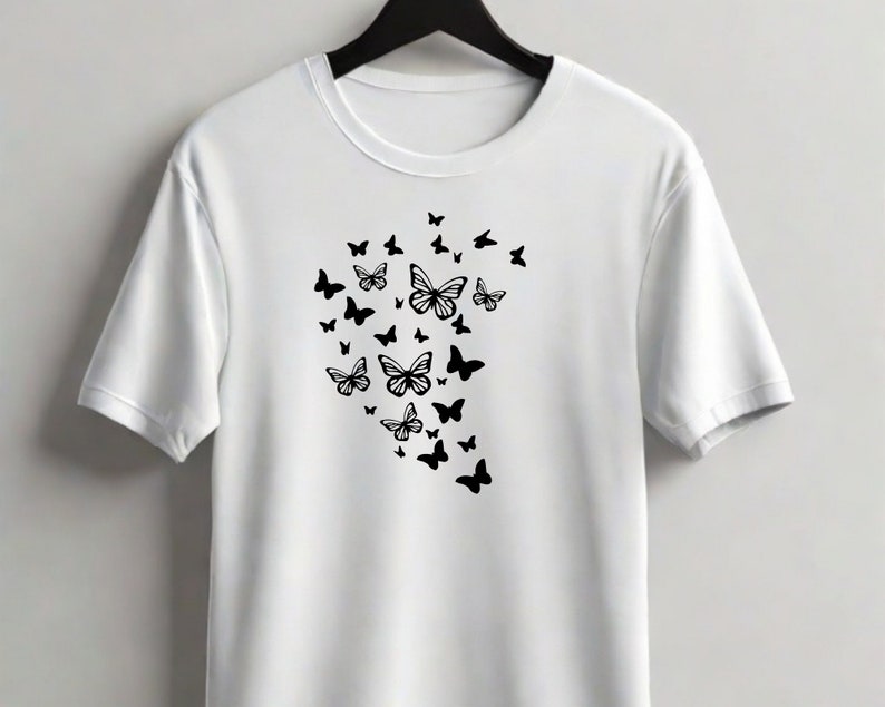 Puede incluir: Camiseta blanca con un dise&ntilde;o de mariposa negra. Las mariposas est&aacute;n agrupadas en forma de coraz&oacute;n.