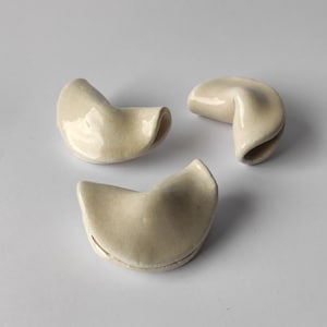 Puede incluir: Tres objetos de cerámica de color blanco roto con forma de galleta de la fortuna.