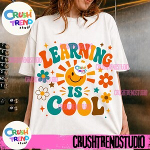 Peut inclure: Un t-shirt blanc à manches courtes avec une impression graphique colorée portant le texte "LEARNING IS COOL" en grandes lettres grasses et multicolores. Le motif comprend une icône de soleil souriant entourée de fleurs stylisées.