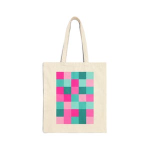 Puede incluir: Un bolso tote de lona beige con un estampado gráfico rectangular central compuesto por una cuadrícula de cuadrados sólidos en tonos rosa fuerte, rosa claro, azul cerceta y verde oscuro. El bolso tiene dos asas largas en la parte superior.