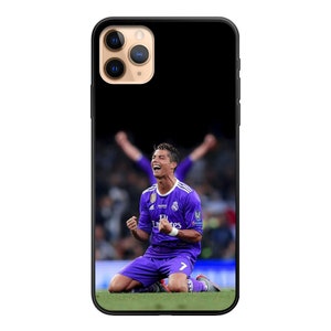 Op de afbeelding: Een paars en wit voetbaltenue met de tekst "Fly Emirates" op de voorkant. Een voetballer draagt het tenue en knielt op het groene gras. De speler viert een doelpunt met zijn armen in de lucht.