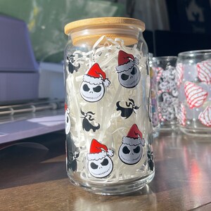 Puede incluir: Un tarro de vidrio transparente con tapa de bamb&uacute;, lleno de papel blanco triturado. El tarro est&aacute; decorado con un patr&oacute;n repetido de Jack Skellington de Pesadilla Antes de Navidad con un gorro de Pap&aacute; Noel.