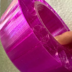 May include: A close-up of a bright purple 3D printed ring. The ring is made of a translucent plastic and has a smooth, glossy finish.