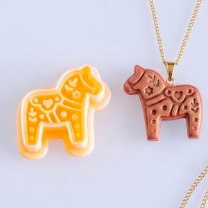Scandi folk horse polymer clay cutter with finished terracotta clay pendant on a gold chain, showing detailed folk style imprint