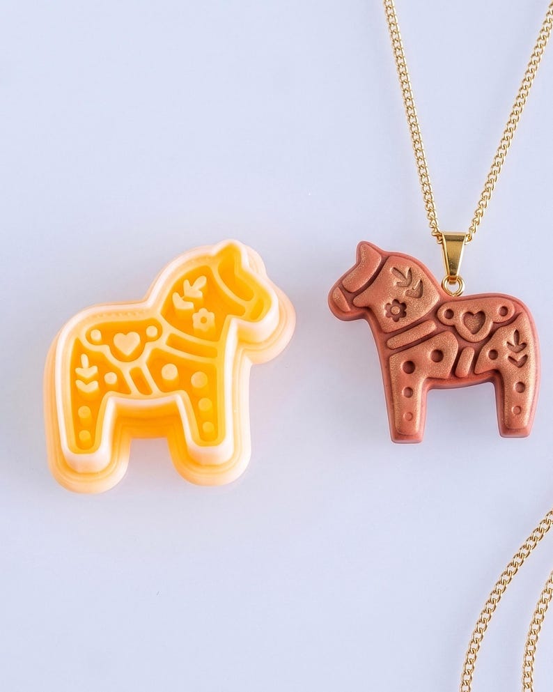 Scandi folk horse polymer clay cutter with finished terracotta clay pendant on a gold chain, showing detailed folk style imprint