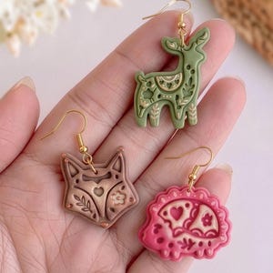 Hand holding scandi folk animal polymer clay earrings including fox, deer and hedgehog designs with soft matte finish
