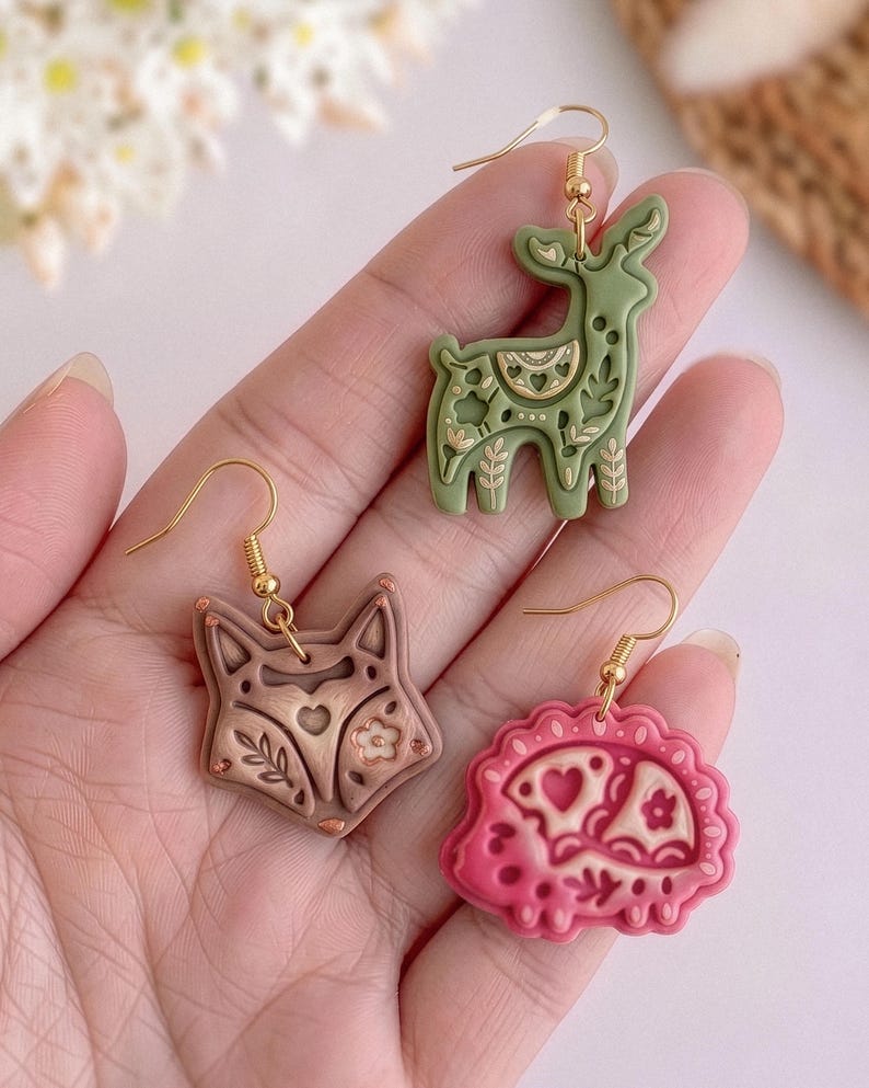 Hand holding scandi folk animal polymer clay earrings including fox, deer and hedgehog designs with soft matte finish