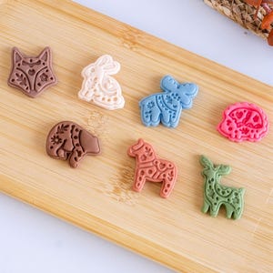 Scandi folk animal polymer clay pieces arranged on a wooden board, showing fox, bunny, moose, bear, horse and deer designs