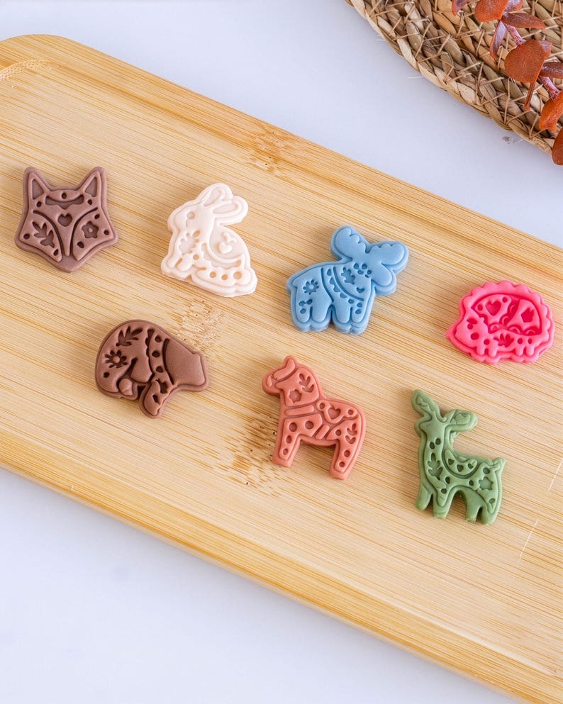 Scandi folk animal polymer clay pieces arranged on a wooden board, showing fox, bunny, moose, bear, horse and deer designs