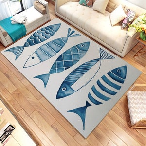 Puede incluir: Una alfombra blanca con un dise&ntilde;o de cinco peces en acuarela azul. Los peces son de diferentes tama&ntilde;os y tienen diferentes patrones. La alfombra est&aacute; sobre un suelo de madera.