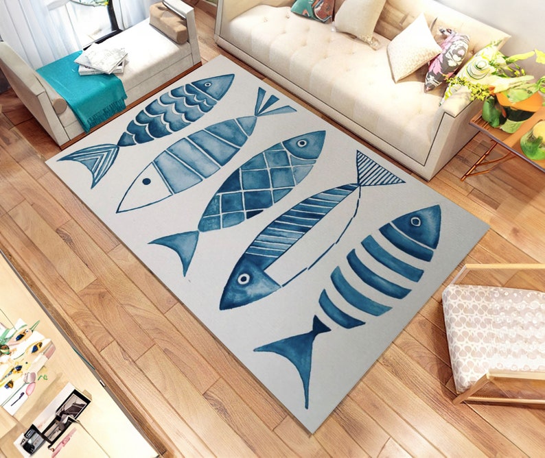 Puede incluir: Una alfombra blanca con un dise&ntilde;o de cinco peces en acuarela azul. Los peces son de diferentes tama&ntilde;os y tienen diferentes patrones. La alfombra est&aacute; sobre un suelo de madera.