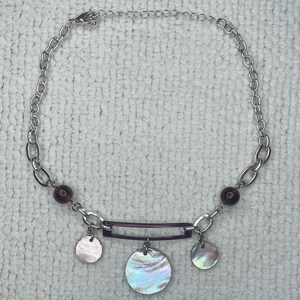 Könnte beinhalten: Eine silberne Kettenkette mit einem violetten Balkenanhänger und drei regenbogenfarbenen runden Muschelanhängern. Die Kette hat zwei dunkelviolette Perlen auf jeder Seite des Balkenanhängers.