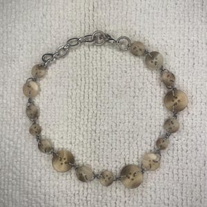 May include: A necklace made of brown buttons and a silver chain. The buttons are strung together with wire.