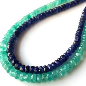 Könnte beinhalten: Zwei Stränge facettierter Edelsteinperlen in Türkis und Marineblau. Die Perlen sind aufgefädelt und bilden ein Halsketten- oder Armbanddesign. Die Edelsteine haben eine polierte, reflektierende Oberfläche.