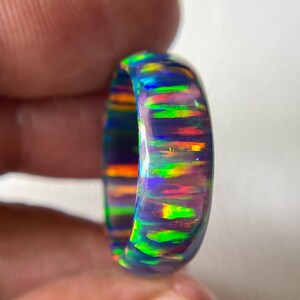 May include: A vibrant opal ring with a dark base color, displaying a spectrum of iridescent colors including blue, green, red, and orange. The polished surface of the ring reflects light, showcasing the play-of-color effect. This gemstone ring is a unique piece of jewelry.