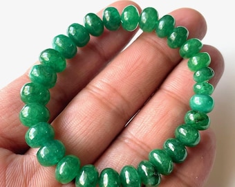 May include: A green beaded bracelet. The bracelet is made of polished, round, emerald-colored beads. The beads are strung together to form a circular shape. The bracelet is shown on a light background.