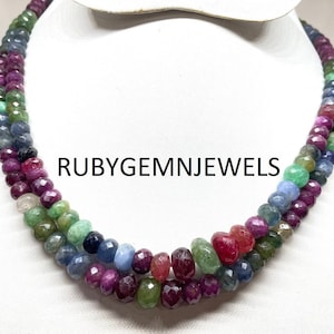 May include: Three-strand necklace composed of faceted gemstones in a gradient of colors, including red, green, blue, and purple. The necklace is displayed on a white mannequin. The text "RUBYGEMNJEWELS" is visible.