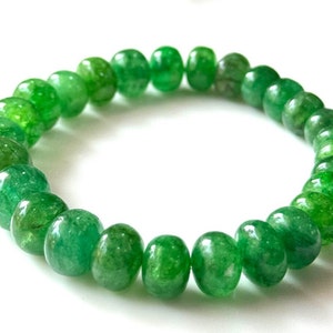 May include: A bracelet made of green, polished beads. The beads are round and vary in shade, from light to dark green. The bracelet is circular and sits against a white backdrop.