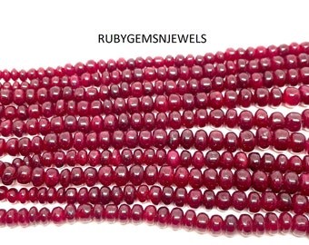 May include: Strands of polished, deep red ruby beads. The beads are small, uniform in size, and strung together. The text "RUBYGEMSNJEWELS" is visible in the upper left corner.