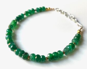 May include: A delicate bracelet featuring faceted, vibrant green emerald beads. The beads are strung together with gold-colored spacers and a silver-colored clasp. The bracelet is designed to be worn around the wrist.