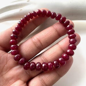 May include: A bracelet made of small, polished, deep red gemstones. The bracelet is circular and appears to be strung on a flexible cord. The gemstones have a rounded shape and a glossy finish, reflecting light.
